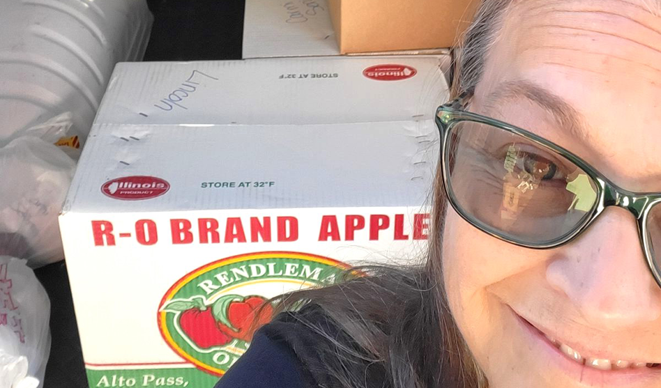 woman smiling with cases of apples behind her